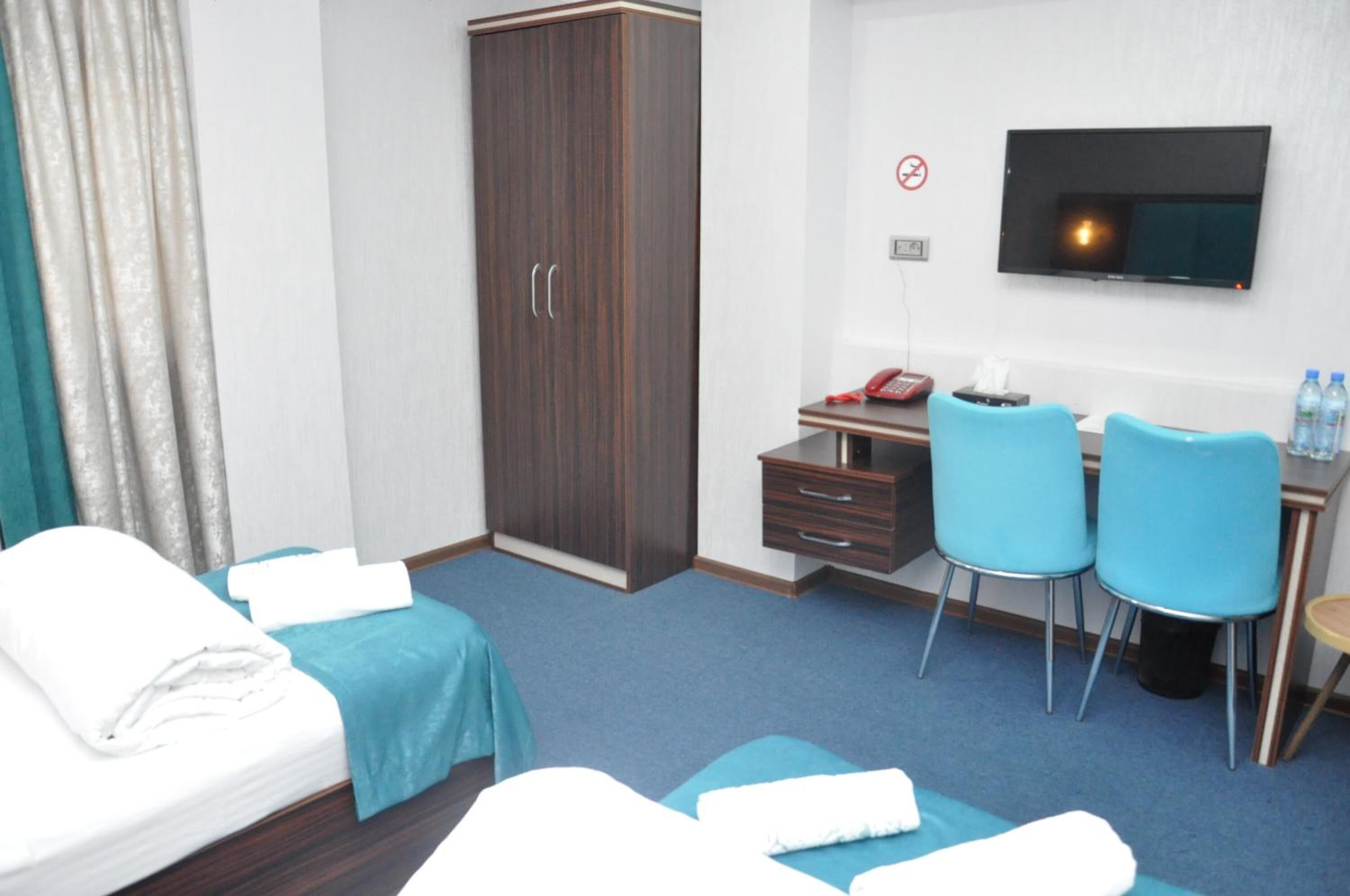 A hotel room with a bed, a desk with two chairs, a wardrobe, a TV, and a no-smoking sign.