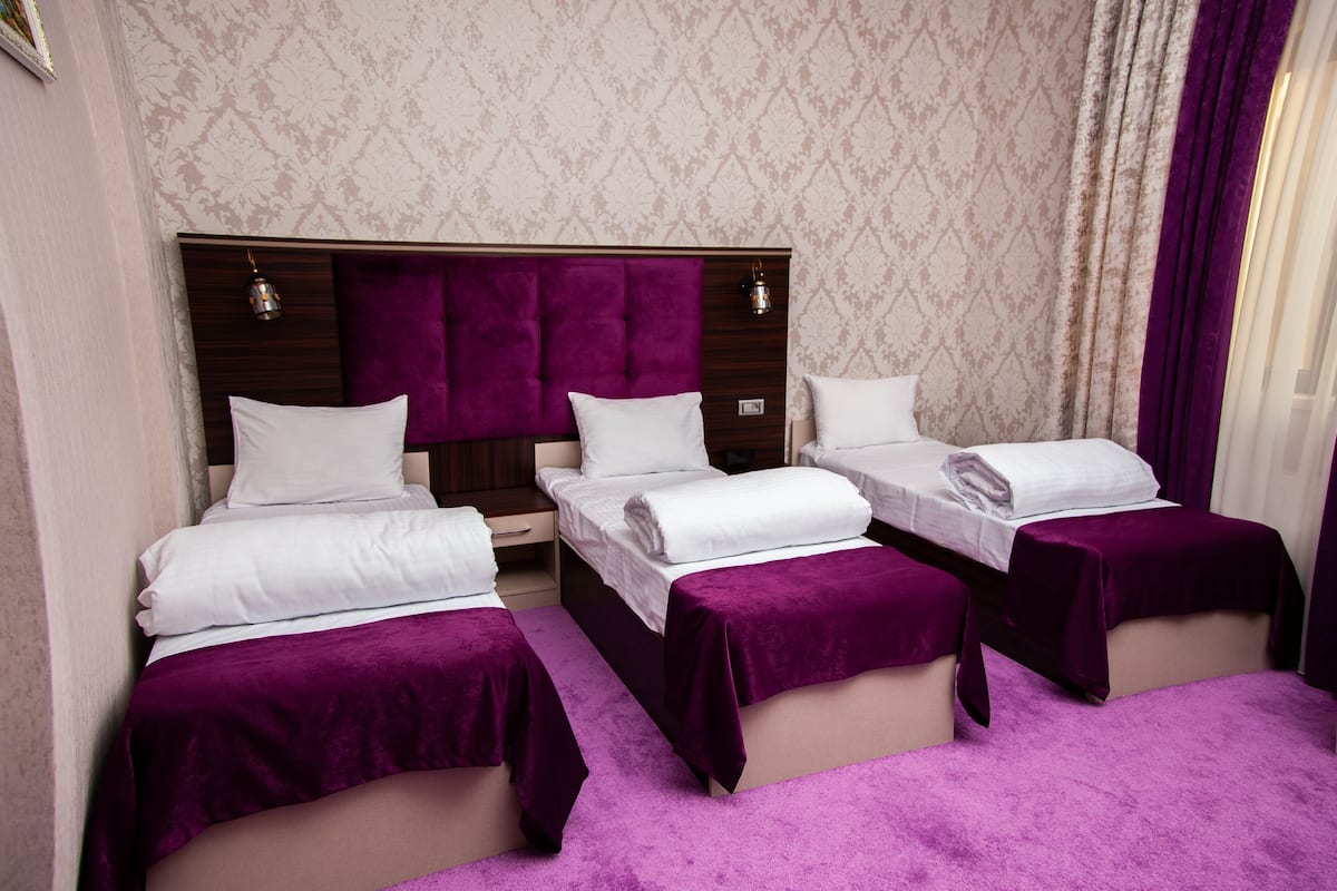 A hotel room with three beds, each with a purple bedspread and white linens.