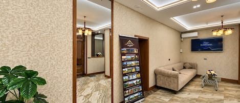 A hotel lobby with a large mirror, a reception desk, a sofa, a TV screen, and a plant.