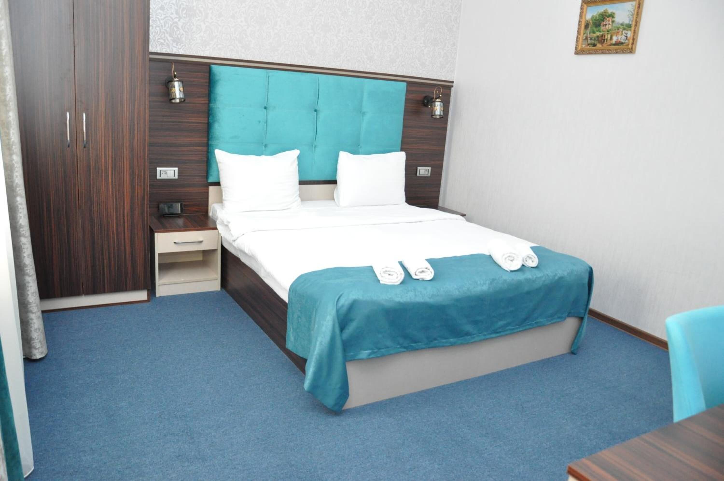A neatly arranged hotel room with a bed, a nightstand, a wardrobe, and a small table.