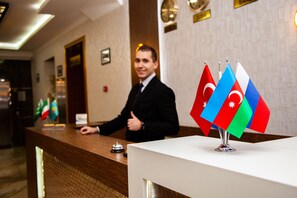 A reception desk with flags of Azerbaijan and Turkey, a man in a suit, and a modern interior with a wooden reception desk and a white counter.