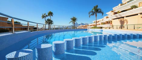 A swimming pool with a tiled design, surrounded by palm trees and a clear sky.