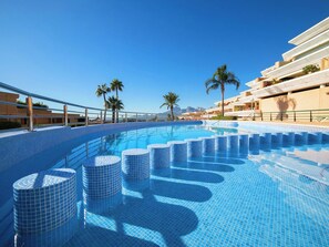 Una piscina con diseño de azulejos, rodeada de palmeras y un cielo despejado.