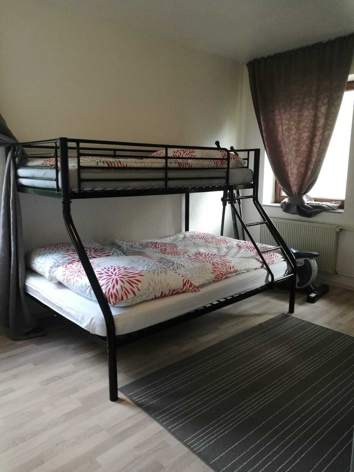 A bunk bed with patterned bedding, a radiator, and a window with curtains.