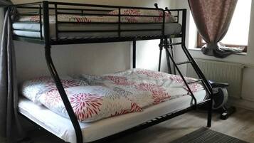 A bunk bed with patterned bedding, a radiator, and a window with curtains.