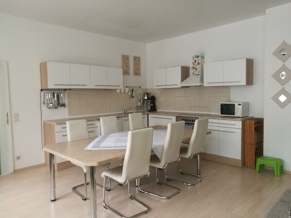 A modern kitchen with white cabinets, a dining table with chairs, a microwave, and a coffee maker.