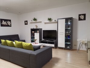 A modern living room with a grey sofa, a flat-screen TV, a white cabinet with glass shelves, and a small white table.