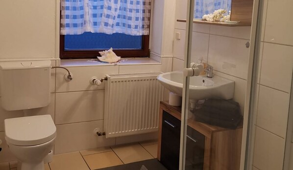 A small bathroom with a toilet, a sink, and a window with a checkered curtain.