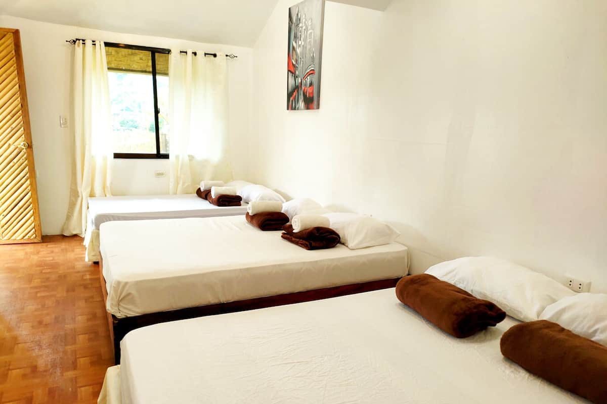 Habitación de hotel con tres camas, cada una con ropa blanca y toallas marrones.