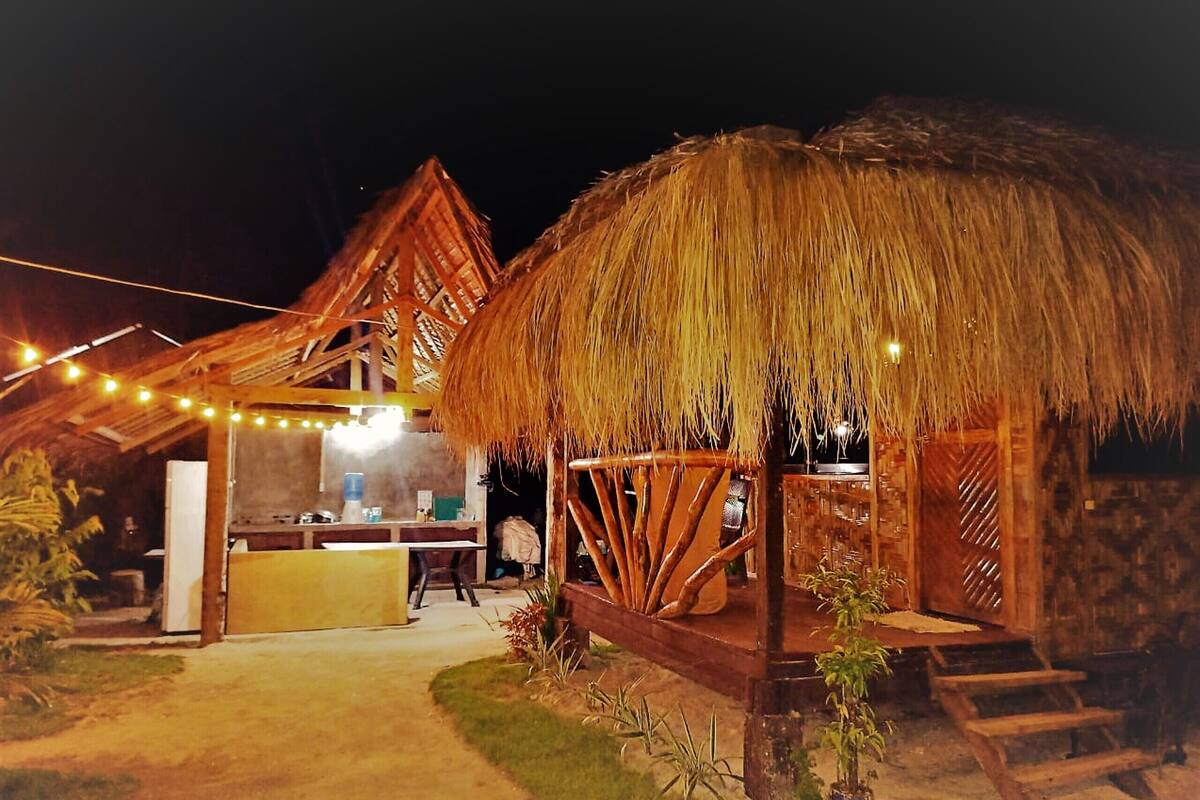 Una estructura de techo de paja con un porche de madera y una zona de bar con luces colgantes.