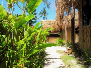 A tropical garden path leading to a thatched-roof building with a wooden exterior. - Siargao Tropic Hostel (General Luna)