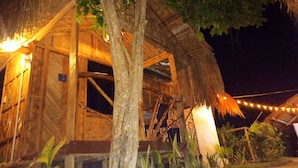 A rustic wooden structure with a thatched roof, surrounded by greenery and string lights. - Siargao Tropic Hostel (General Luna)