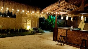 A thatched-roof structure with a bar area featuring a woven backrest and stools. - Siargao Tropic Hostel (General Luna)