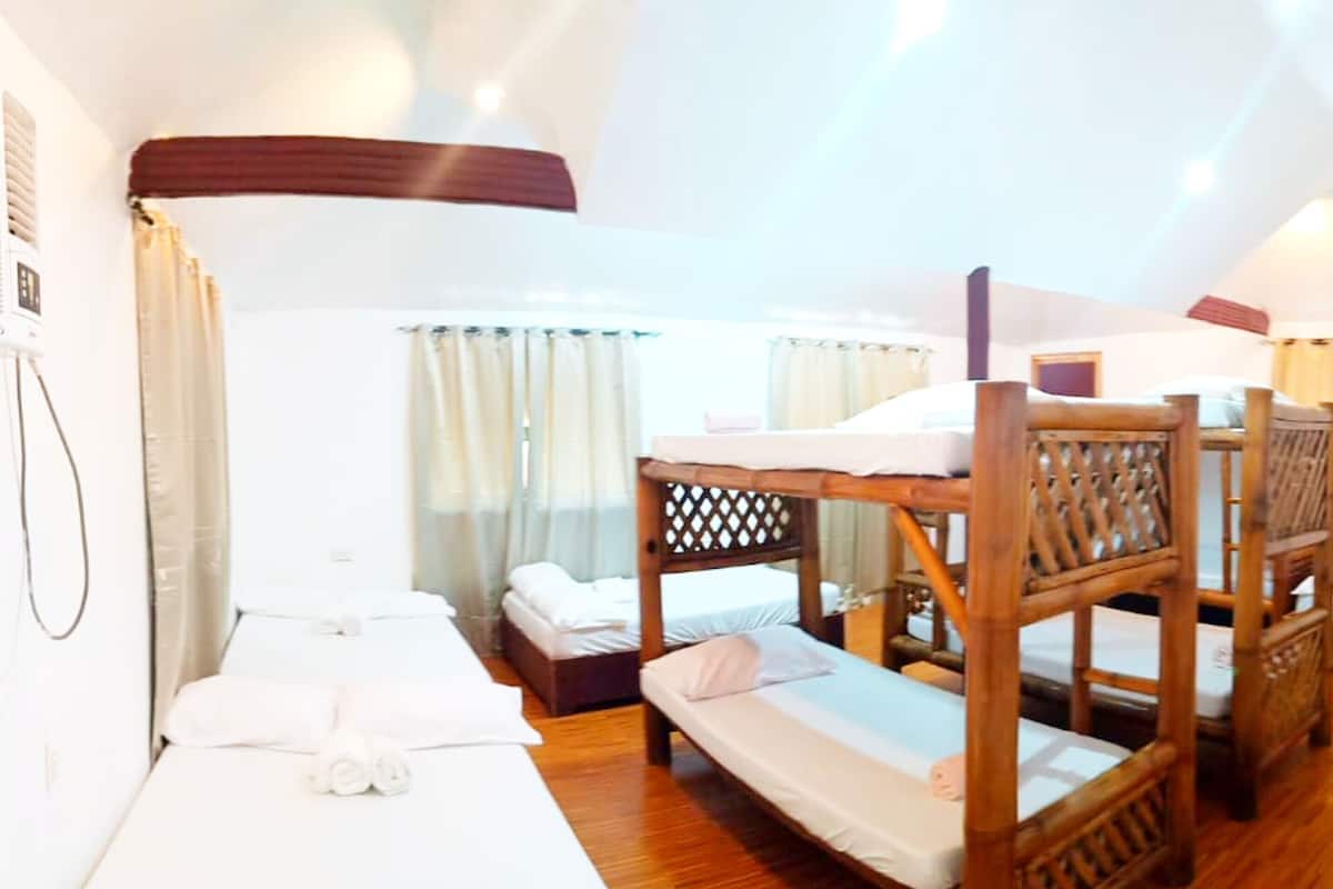 Una habitación con literas, una silla de madera, una mesita pequeña y una cama con colchón y almohadas blancos.