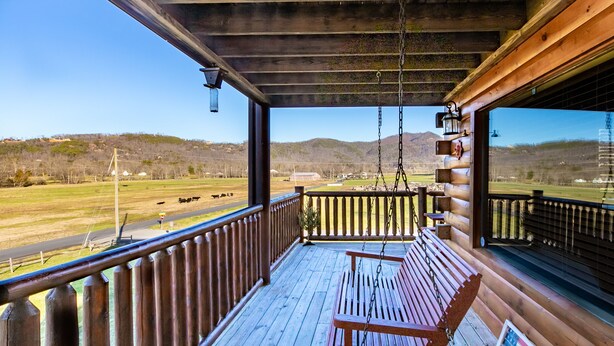 Een houten veranda met een schommel, uitzicht op een landelijk landschap en een kleine Amerikaanse vlag.