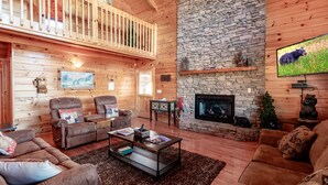 Un intérieur de chalet chaleureux avec une cheminée en pierre, des murs en bois et un balcon.