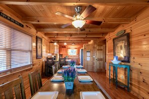 A wooden cabin interior with a dining table set for four, a ceiling fan, and a framed picture on the wall. - Welcome 2026 - 12 mins to Parkway. Great Views.No steep roads. HotTub PoolTable (Sevierville)