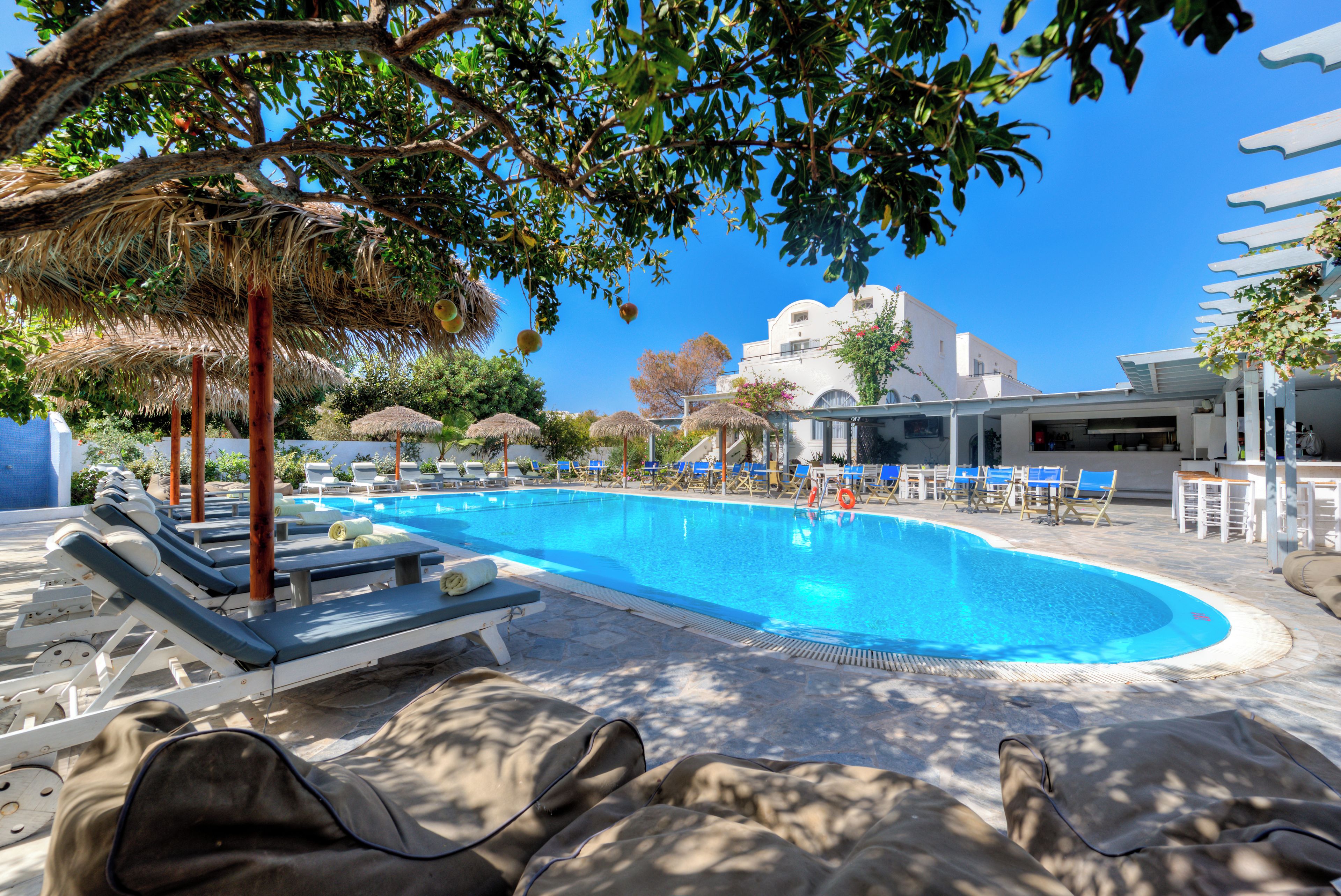 A swimming pool with lounge chairs and umbrellas, surrounded by trees and a building in the background.