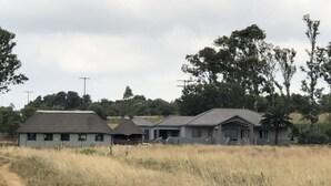 A row of three houses with a dirt path in front, surrounded by tall grass and trees. - Spendpenny Guest Farm (Kgetlengrivier)