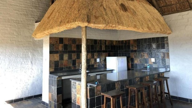 A kitchen with a large island, black and brown tiles, a thatched ceiling, and a white refrigerator. - Spendpenny Guest Farm (Kgetlengrivier)