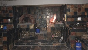 A stone-floored room with a brick oven and a fire burning. - Spendpenny Guest Farm (Kgetlengrivier)