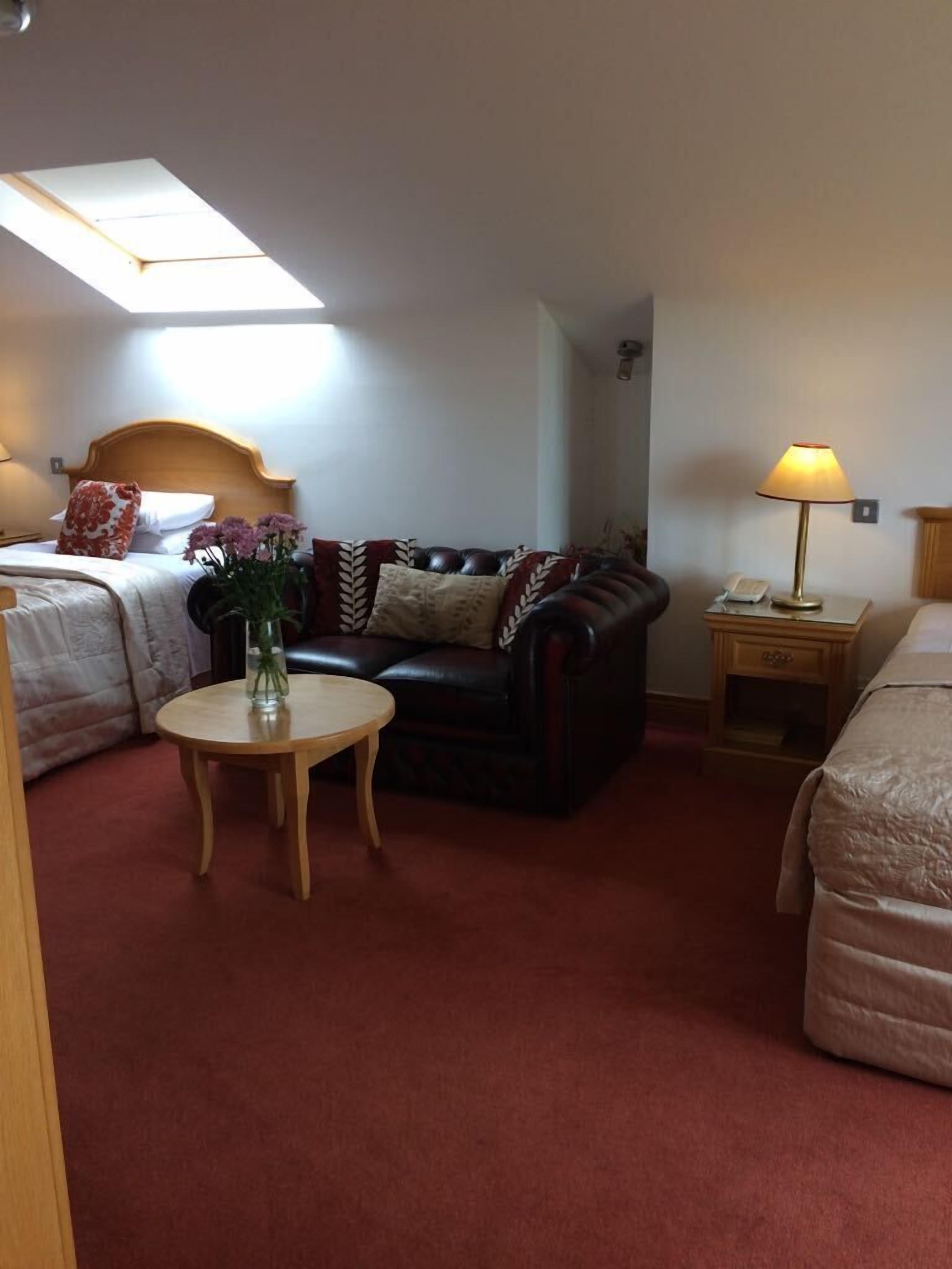 A hotel room with a bed, a sofa, a small table with a vase of flowers, a lamp, and a ceiling light.