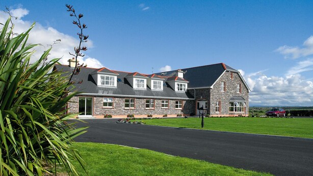 A large, two-story stone house with a sloped roof and a well-maintained lawn. - Cashen Course House (Ballybunion)