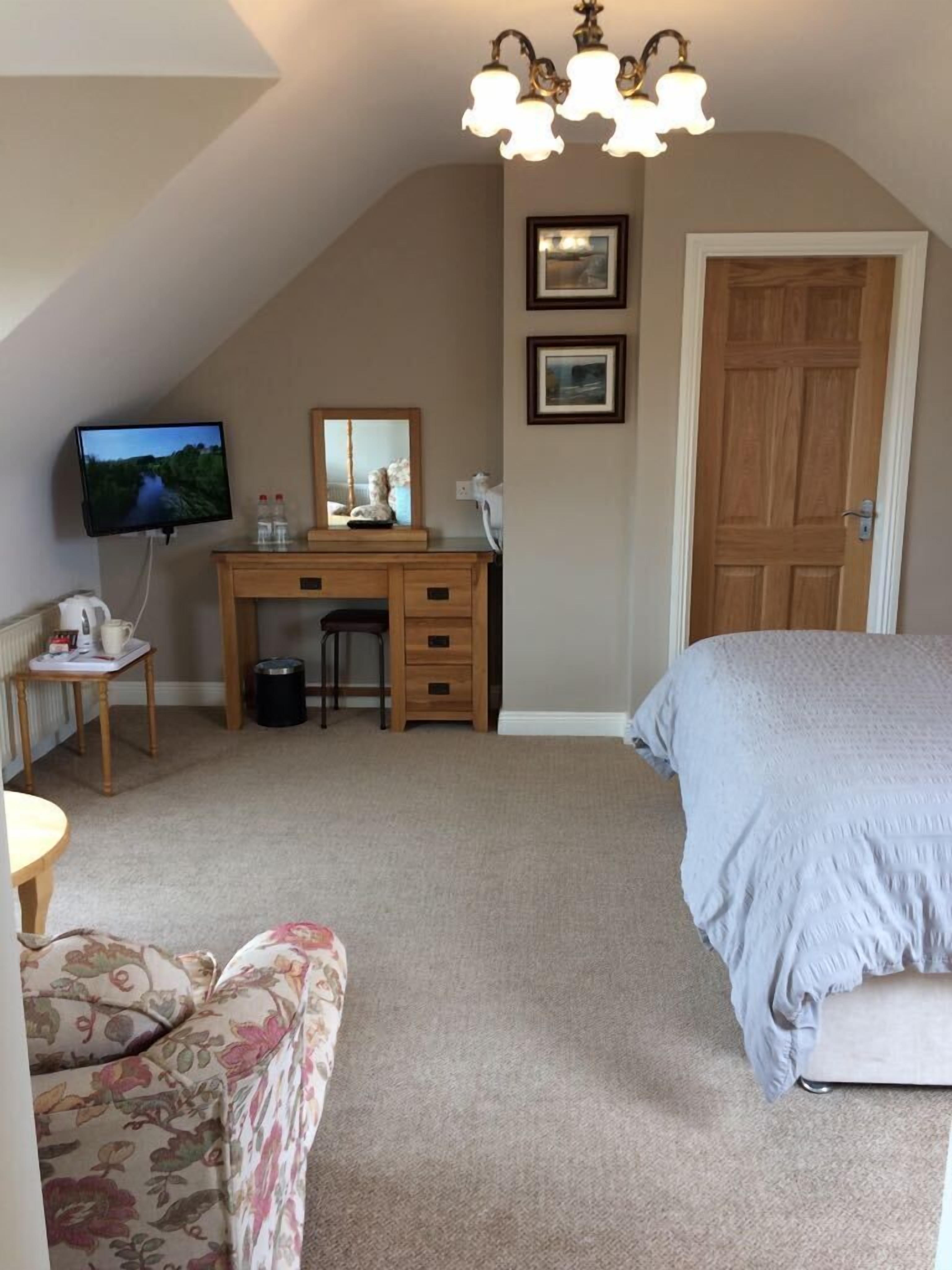 A bedroom with a bed, a desk with a computer, a chair, a television, and a door.