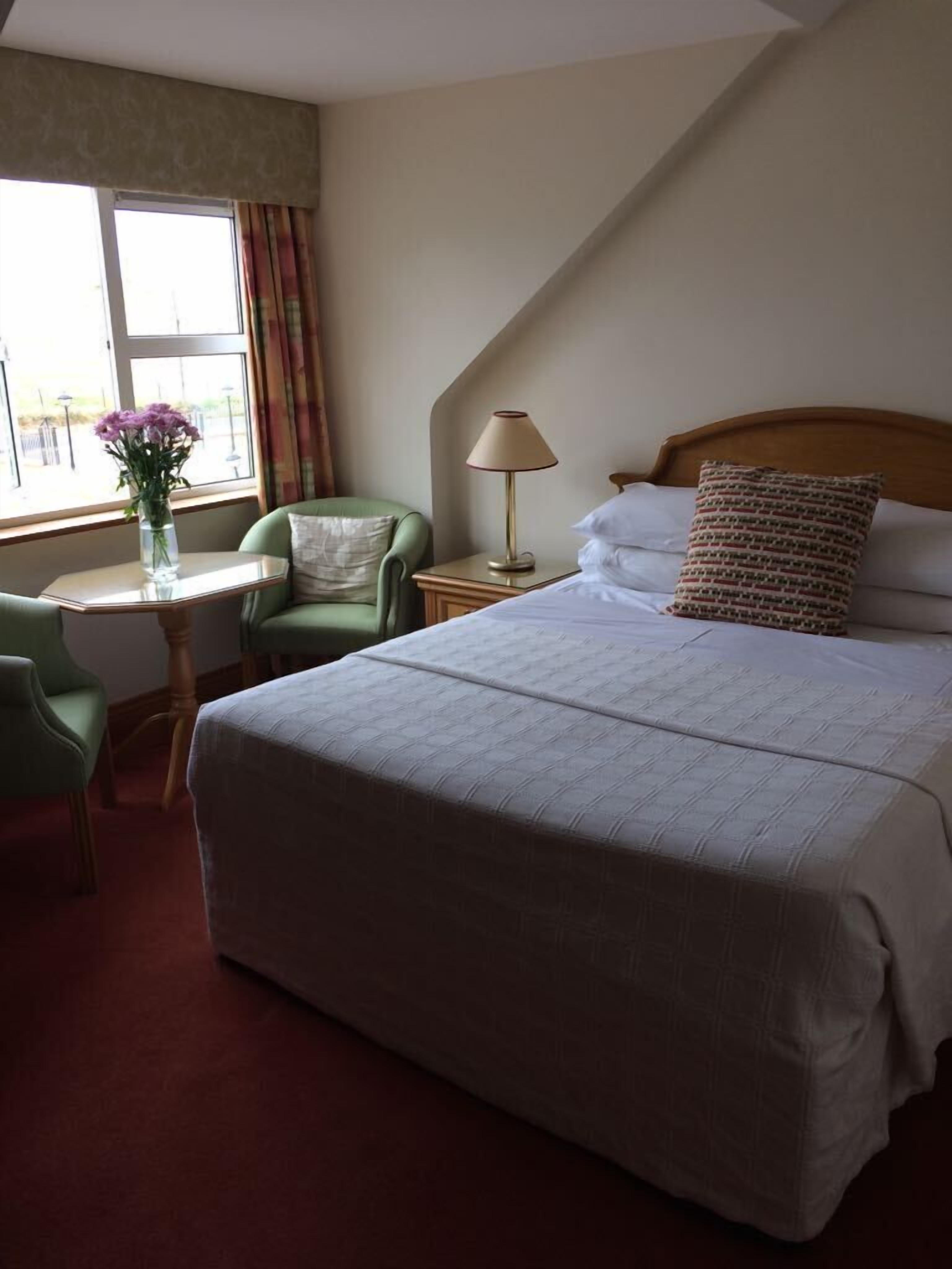 A hotel room with a large bed, a desk with a chair, a lamp, and a window with curtains.