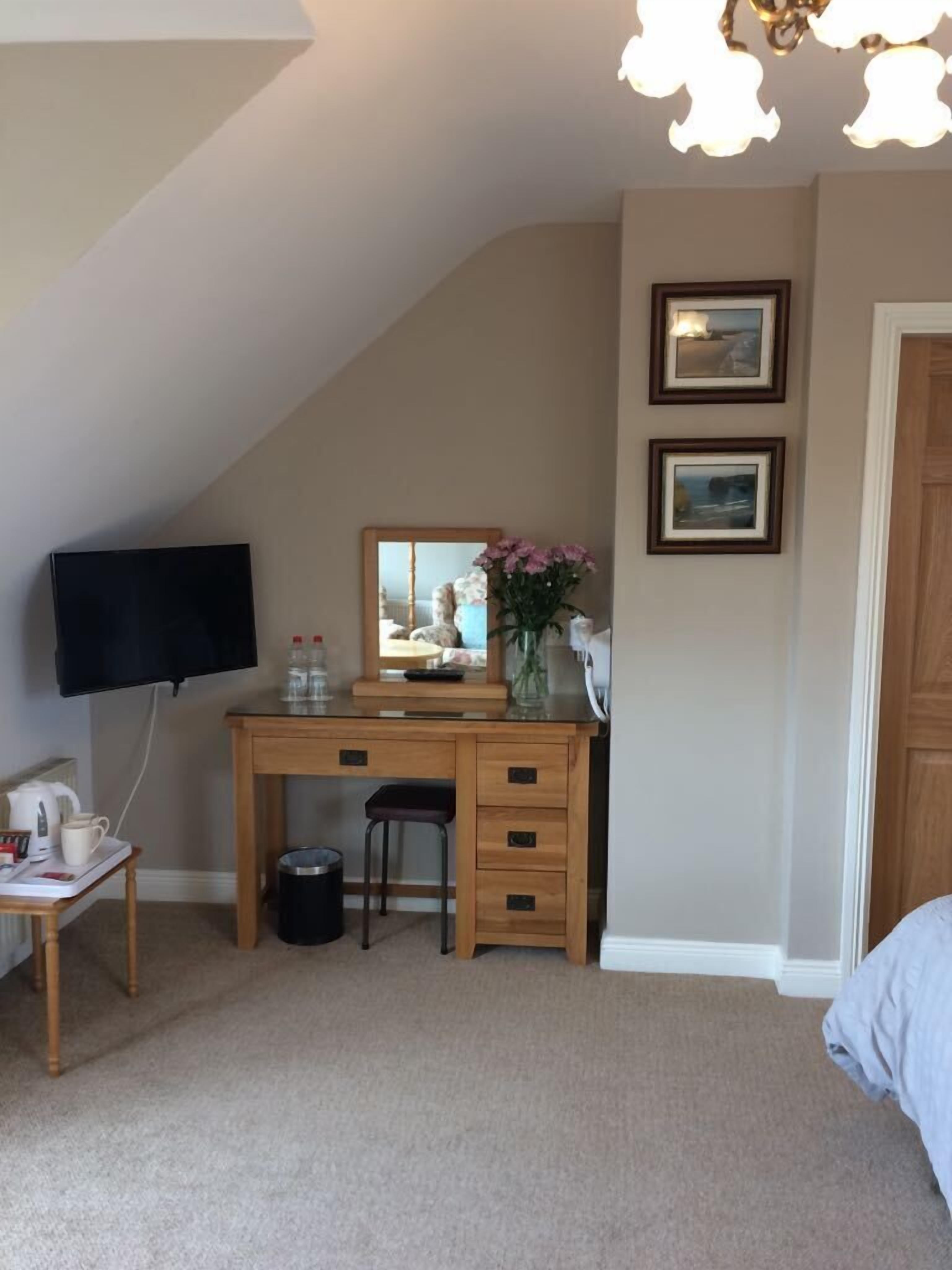 A bedroom with a sloped ceiling, a desk with a mirror, a chair, a bed, and two framed pictures on the wall.