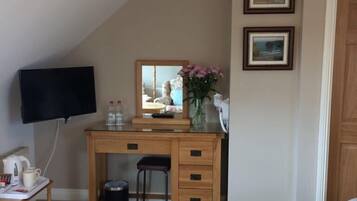 A bedroom with a sloped ceiling, a desk with a mirror, a chair, a bed, and two framed pictures on the wall.