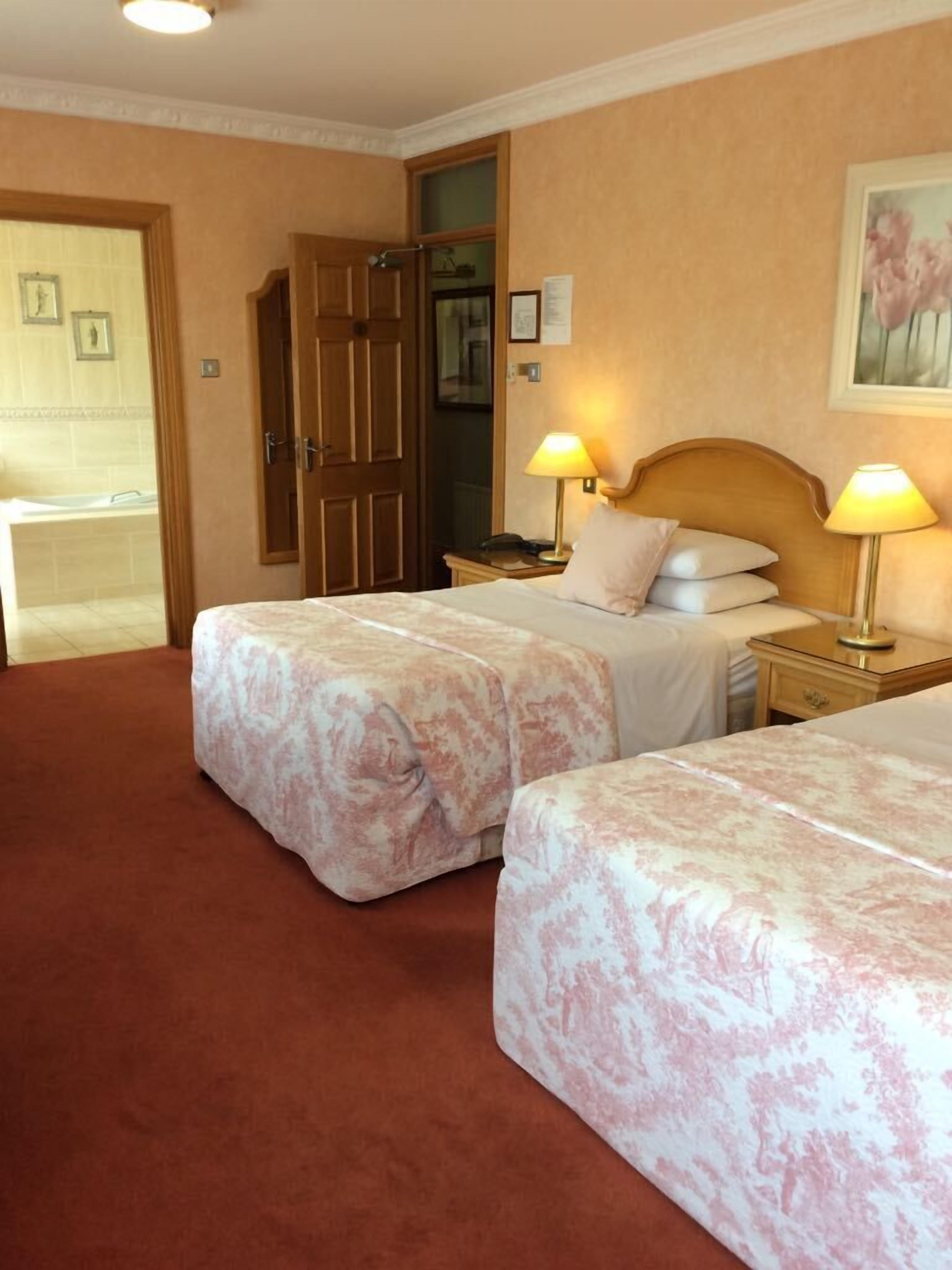 Een hotelkamer met twee bedden, een houten kledingkast, een badkamer met een bad en een schilderij aan de muur.