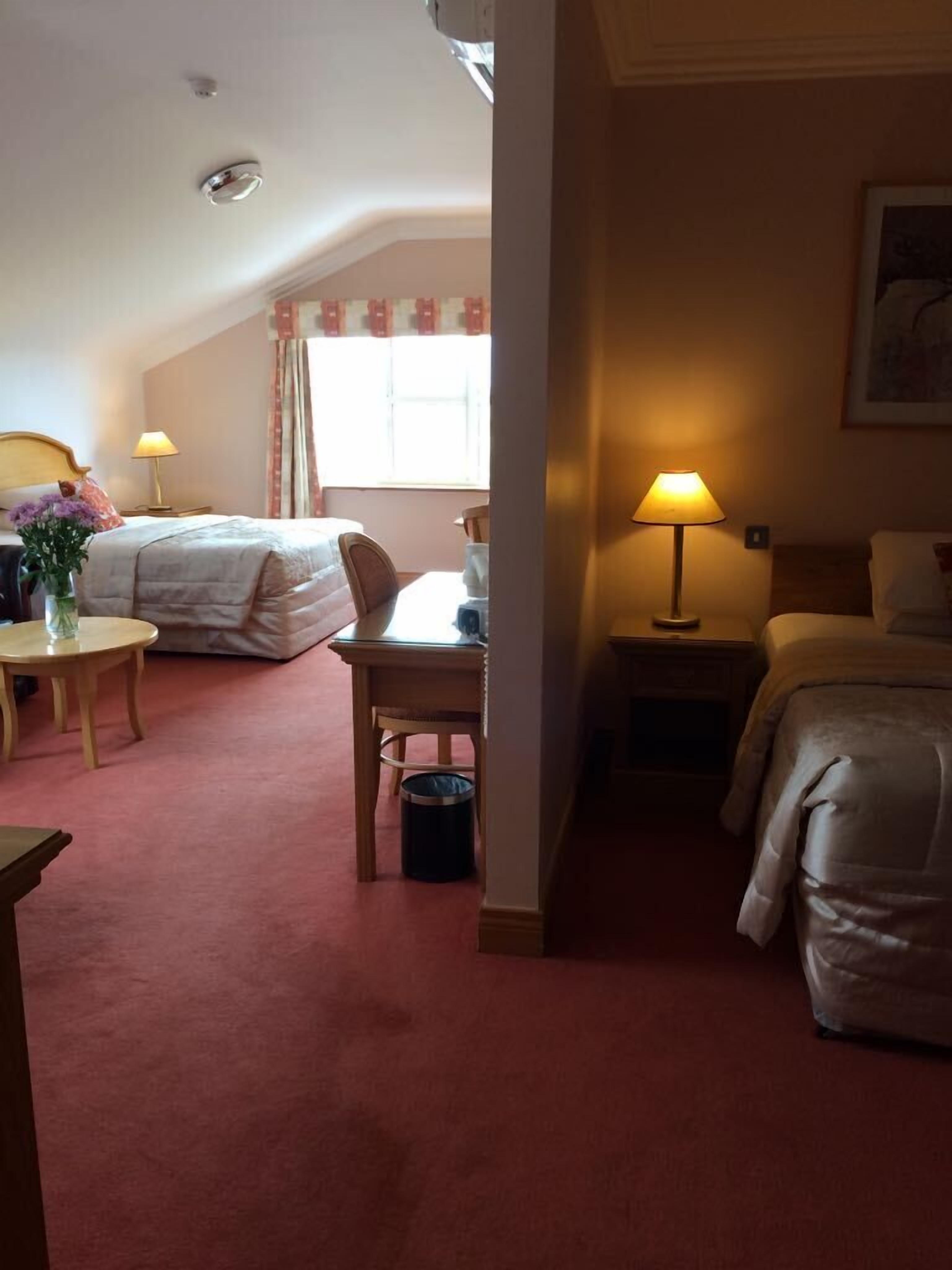 Una habitación de hotel acogedora con cama, escritorio, silla, lámpara y una mesita.
