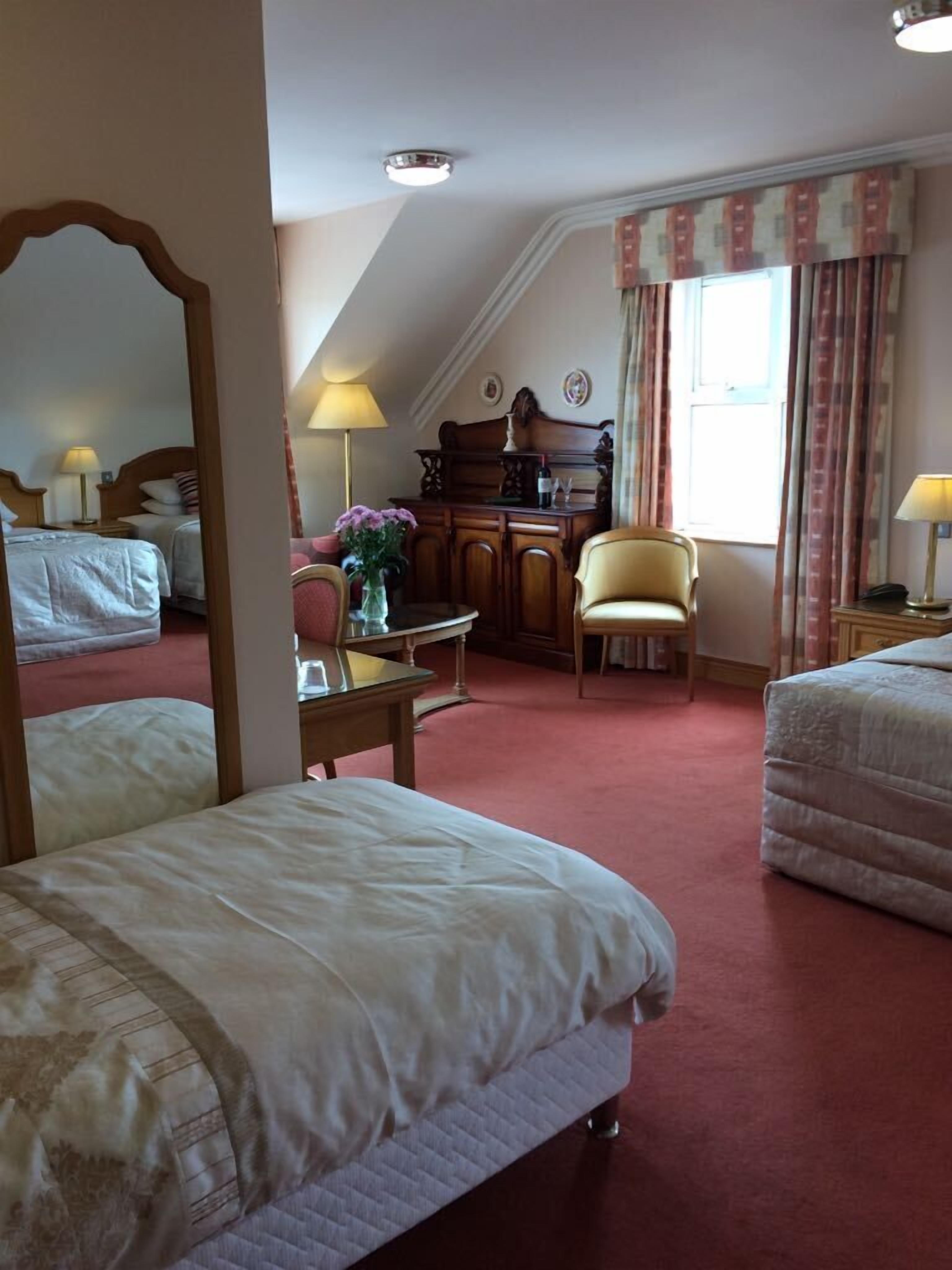 Une chambre d’hôtel avec deux lits, un bureau avec une lampe, une chaise et un grand miroir.