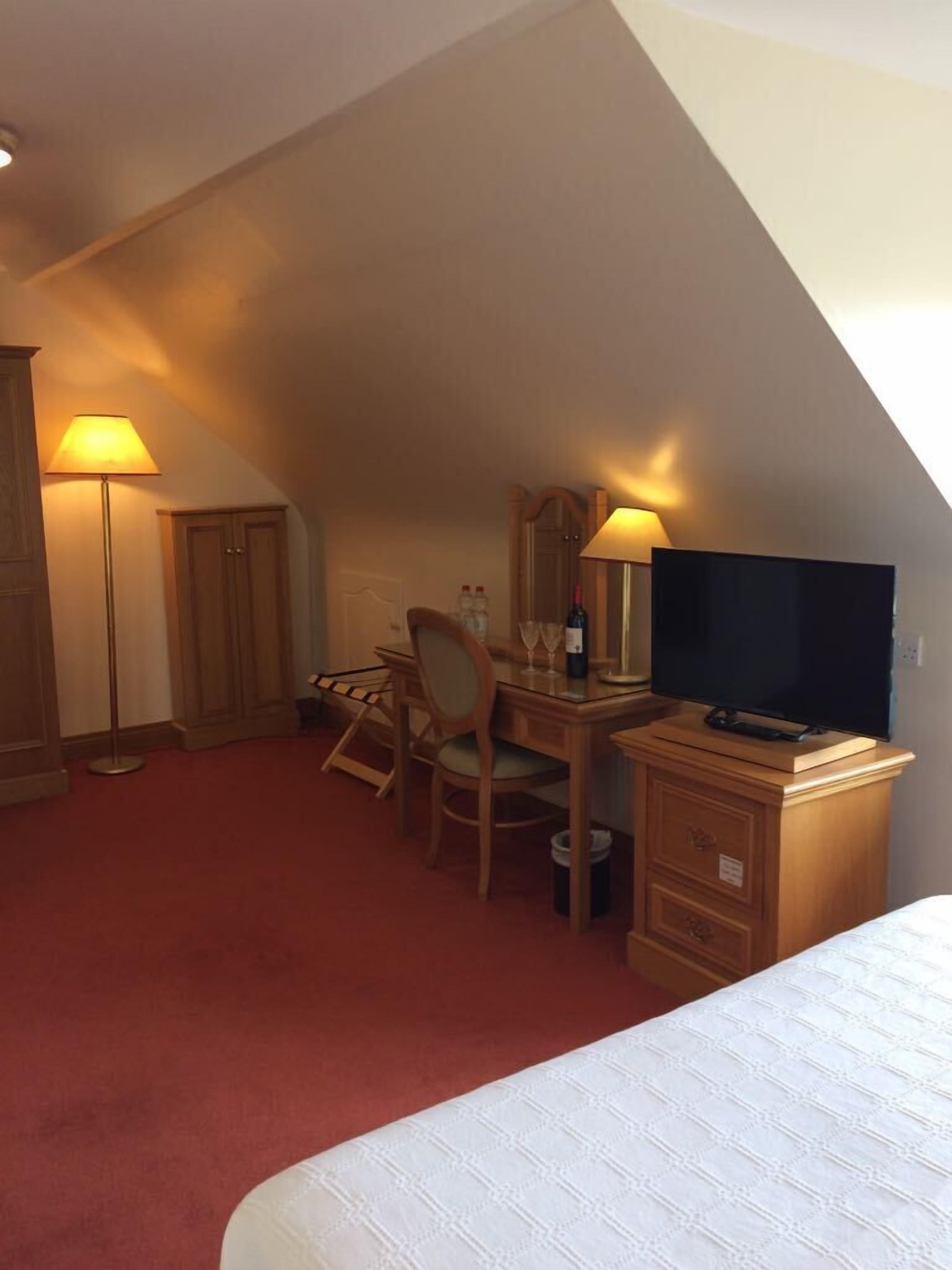 A hotel room with a bed, desk, chair, television, and a lamp.