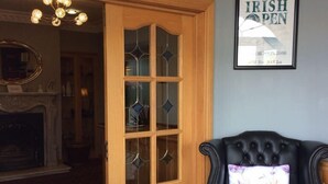 A room with a black leather armchair, a checkered floor, a wooden door with glass panels, and a framed sign on the wall. - Cashen Course House (Ballybunion)