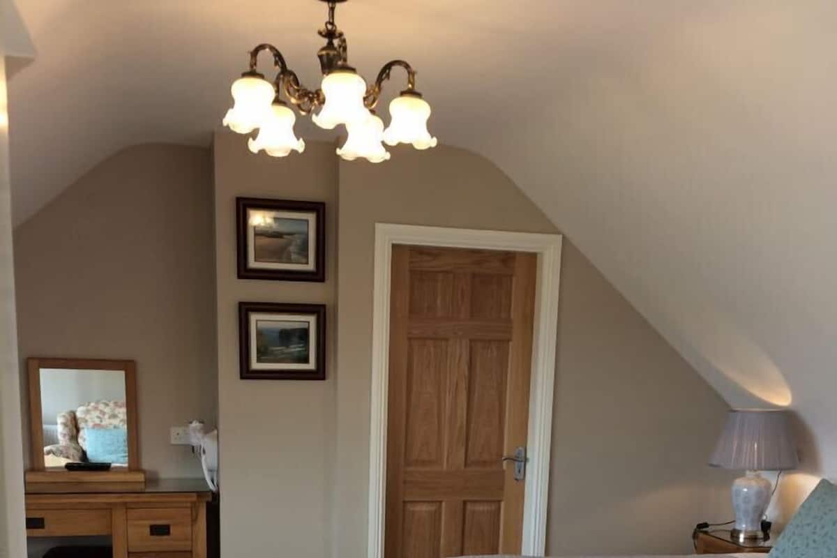 Un dormitorio con cama, escritorio, silla, puerta y candelabro.