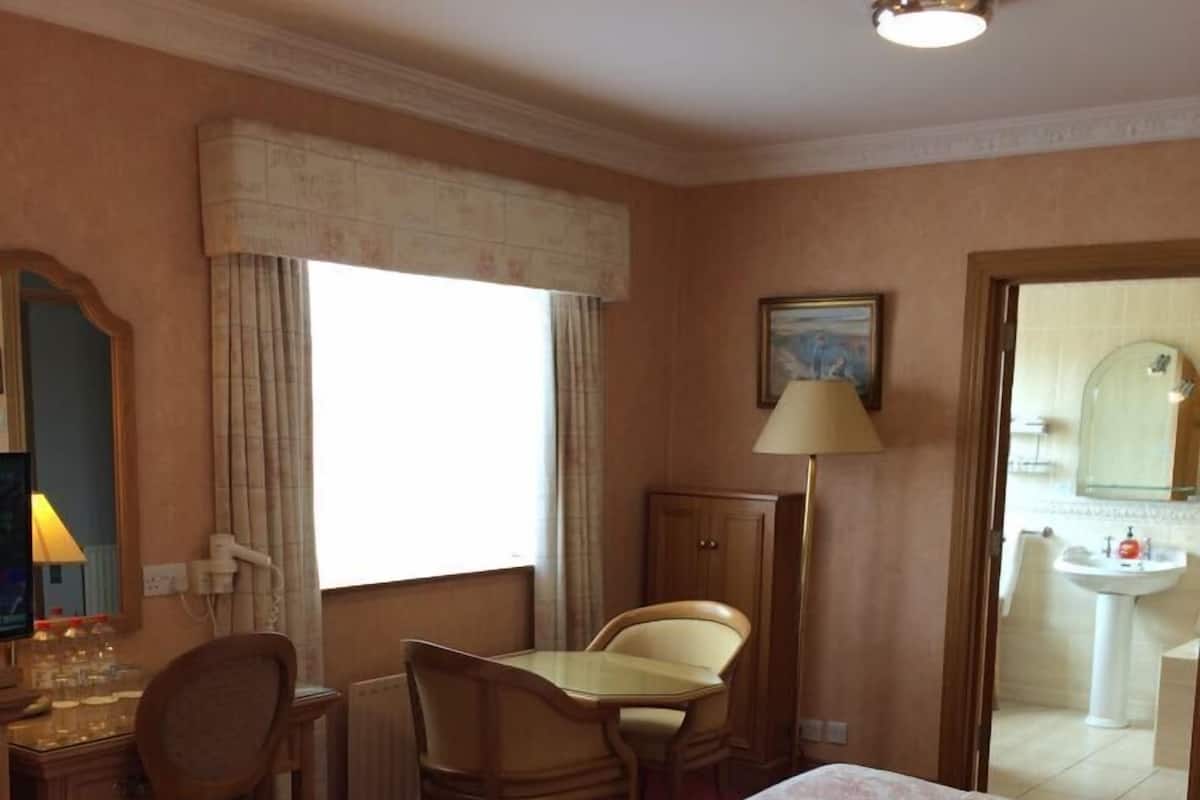 Una habitación de hotel con dos camas, un escritorio, una silla, una lámpara y una ventana.