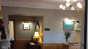 A hotel lobby with a red patterned carpet, wooden paneling, a chandelier, a desk with a lamp, and a vase with flowers. - Cashen Course House (Ballybunion)