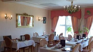 A dining area with multiple tables set for service, wooden chairs, and a chandelier. - Cashen Course House (Ballybunion)