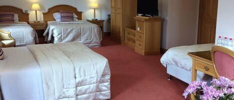 A hotel room with two beds, a desk, a chair, a TV, and a vase with flowers.