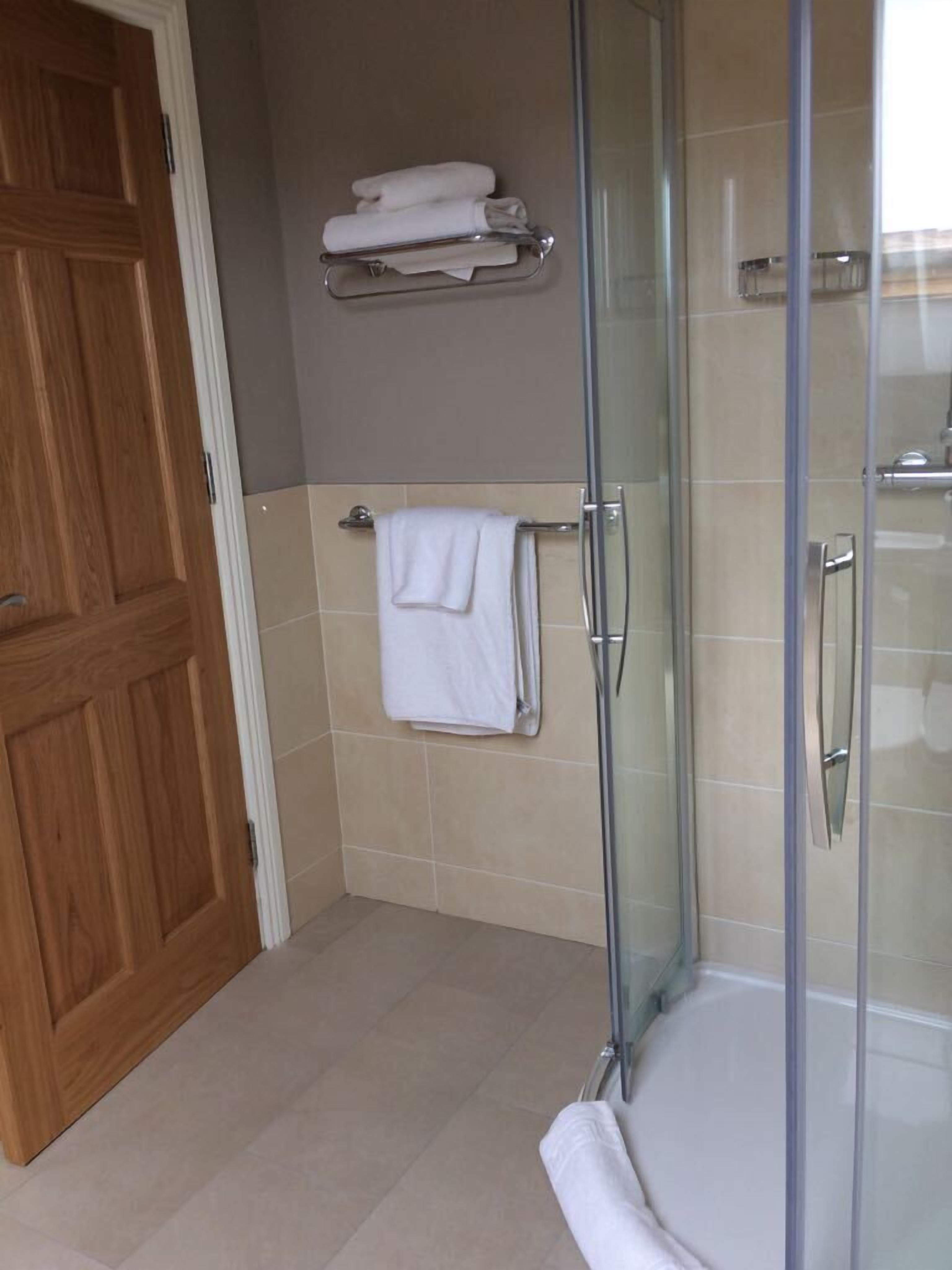 A bathroom with a glass shower enclosure, a wooden door, and a towel rack with folded towels.