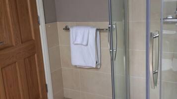 A bathroom with a glass shower enclosure, a wooden door, and a towel rack with folded towels.
