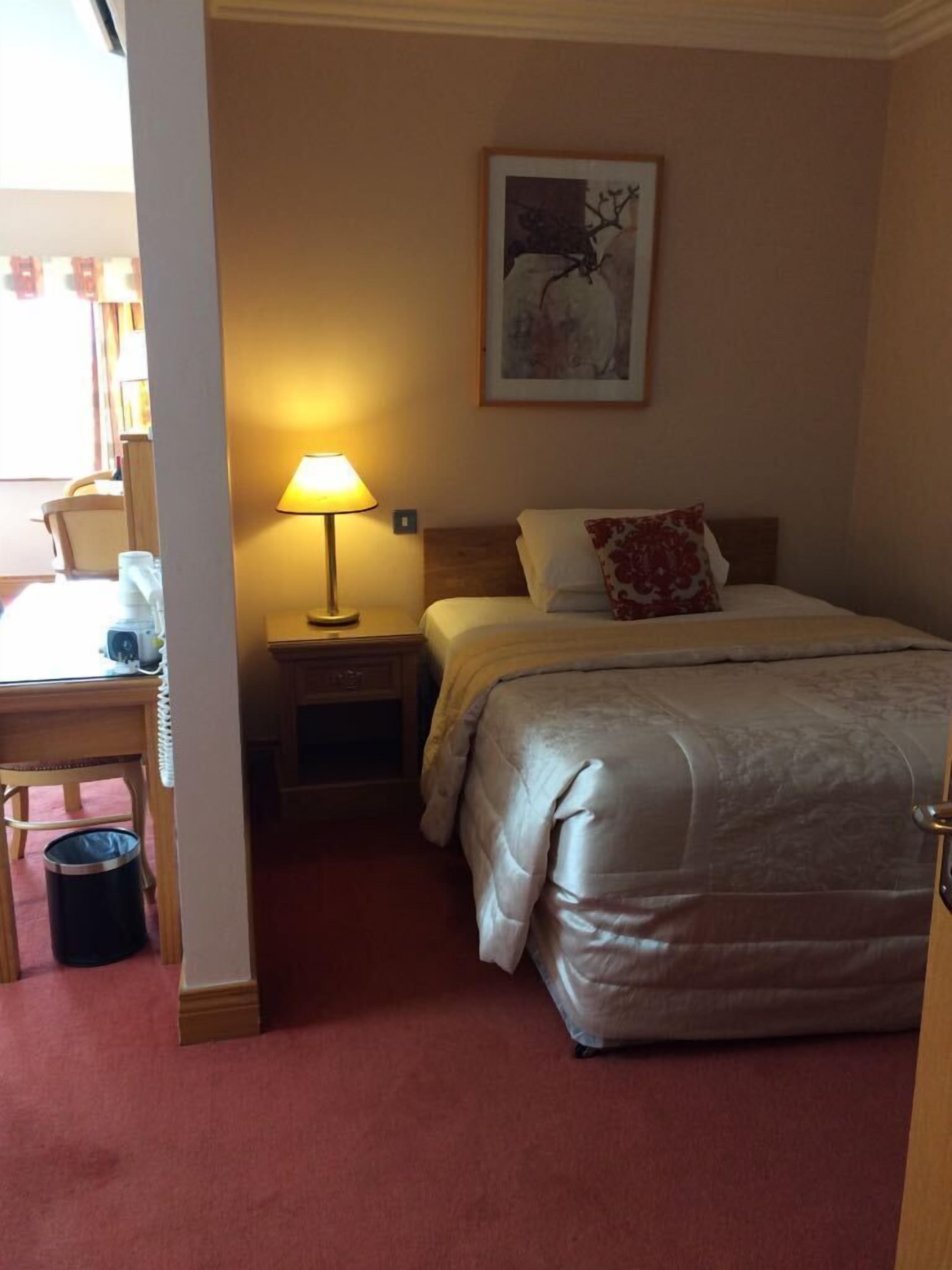 Una habitación de hotel con una cama, una mesita de noche con lámpara, una silla y un cuadro en la pared.