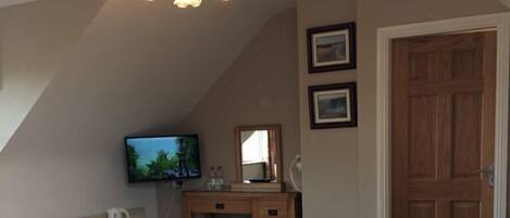A bedroom with a large bed, a desk with a mirror, a television, and a wooden door.
