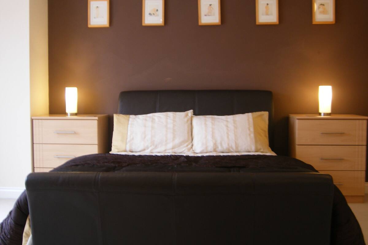 A neatly made bed with a dark headboard, two bedside tables with lamps, and four framed pictures on the wall.