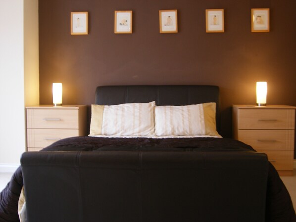A neatly made bed with a dark headboard, two bedside tables with lamps, and four framed pictures on the wall.