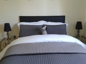 A neatly made bed with a dark headboard, two bedside lamps, and a small decorative dog figurine on the pillow.