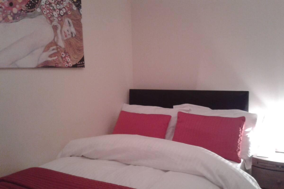 A bed with white and red bedding, a black headboard, and a painting on the wall.