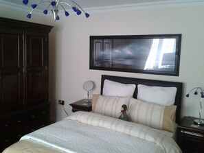 A bedroom with a bed, a nightstand, a dresser, a mirror, and a picture frame on the wall.